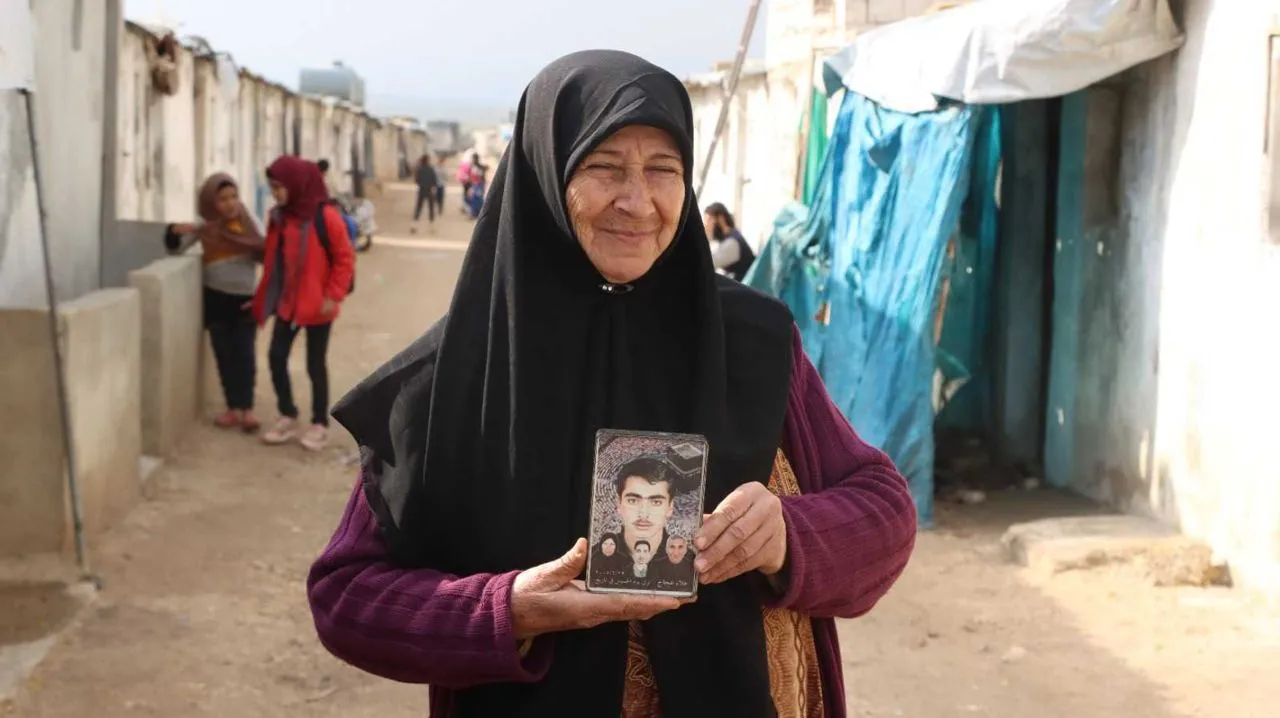 سيدة في أحد مخيمات الشمال السوري وهي تحمل ذكريات زوجها وابنها اللذين فقدتهما خلال سنوات الحرب