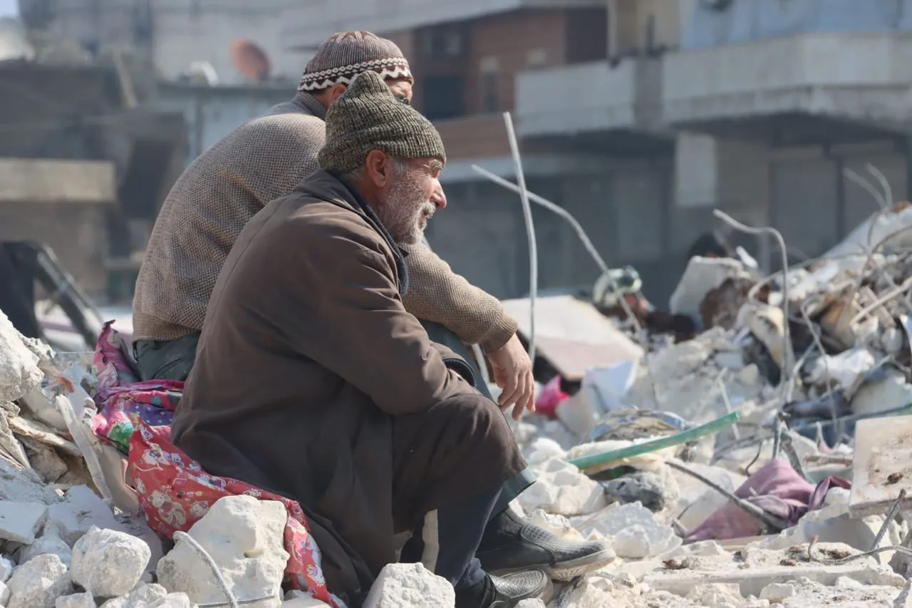 رجلان يجلسان على الأنقاض التي خلفها الزلزال في بلدة عزمارين بريف إدلب