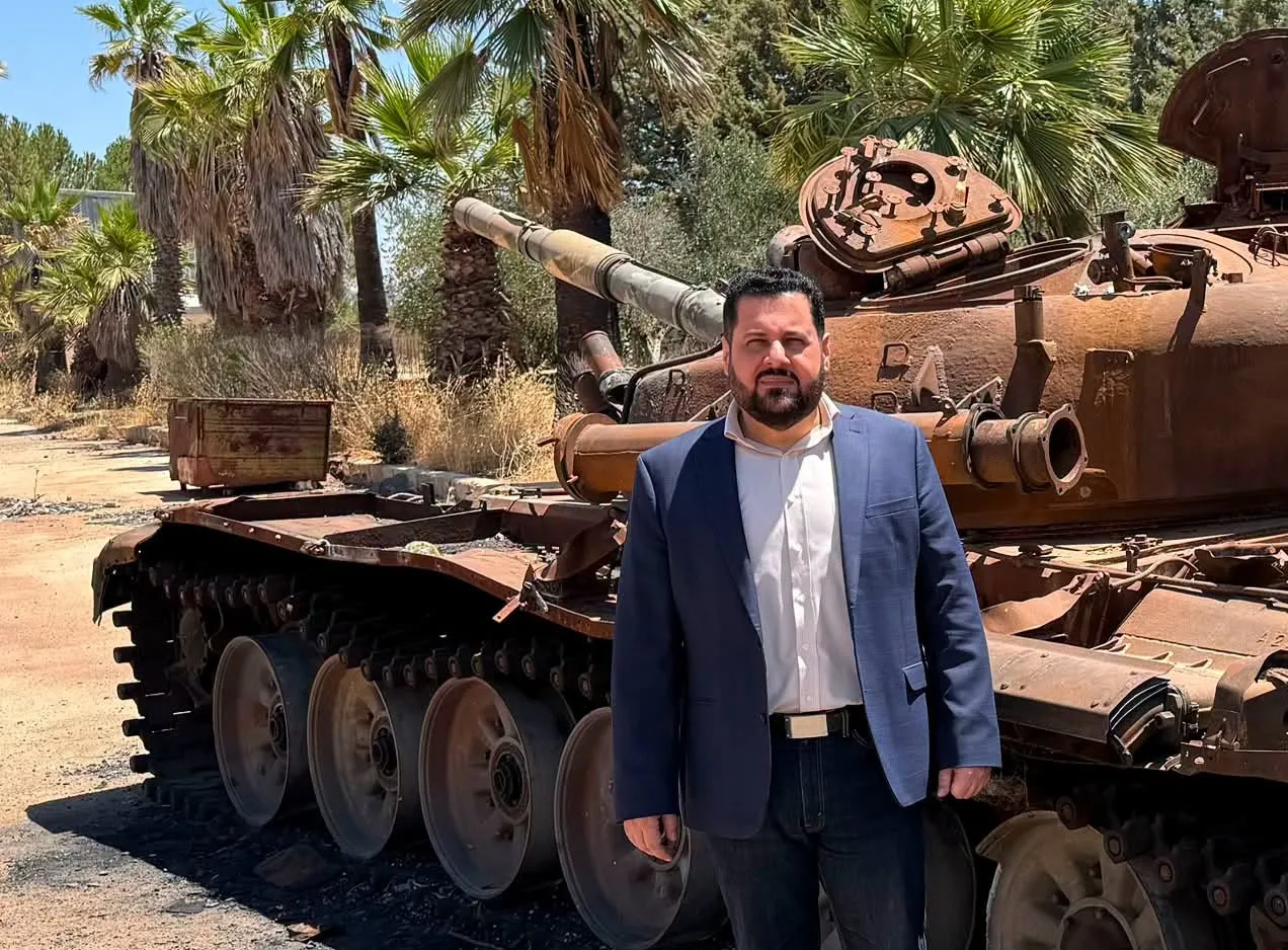 ماهر شرف الدين يقف متفاخراً أمام إحدى دبابات الجيش العربي السوري التي استهدفها قصف إسرائيلي في السويداء.